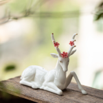 White ceramic deer tea pet displayed on wooden windowsill with green plant background