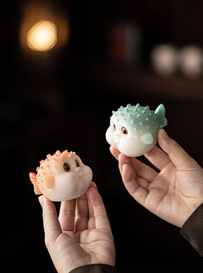 Orange and blue color changing pufferfish tea pets held in hands showing their cute expressive faces