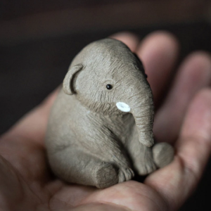 Hand holding mini cute elephant tea pet showing compact palm size