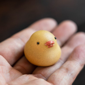 Mini Yixing purple clay duck tea pet held in palm showing tiny size