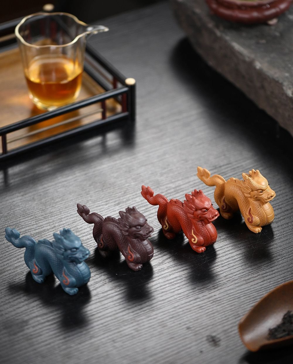 Four color variants of zisha dragon tea pets arranged on a tea tray