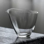 Clear glass gong dao bei tea pitcher next to teacup on wood tea mat