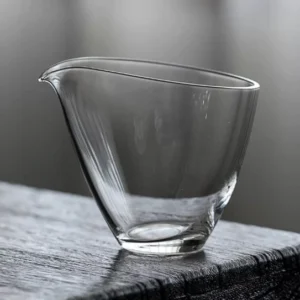 Clear glass gong dao bei tea pitcher next to teacup on wood tea mat