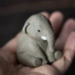 Hand holding palm-sized mini cute elephant tea pet showing compact size
