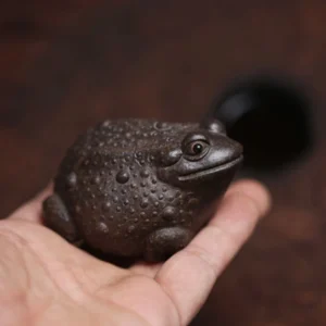 Hand holding handcrafted Yixing zisha lucky toad tea pet showing size and clay texture