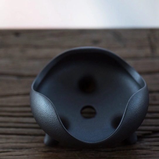 side view of matte black ceramic loose leaf tea strainer on three-legged stand
