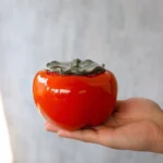Full view of persimmon shaped ceramic tea jar on wood background