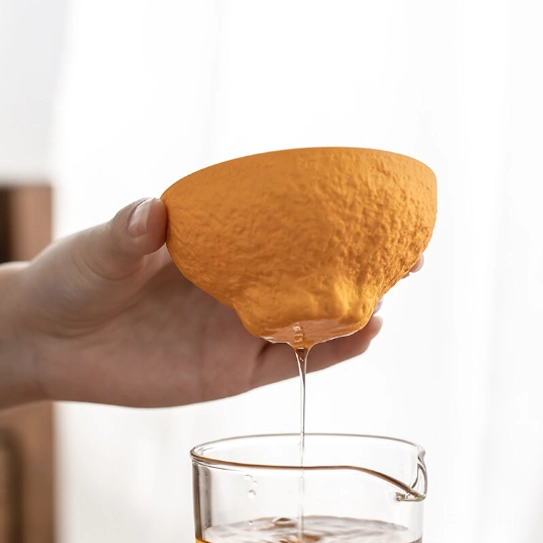 portable orange ceramic tea strainer held in hand to show size