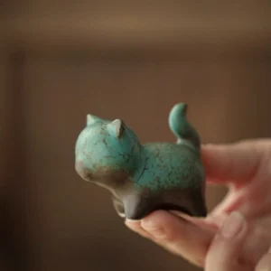 Hand holding small turquoise ceramic cat tea pet showing compact handheld size