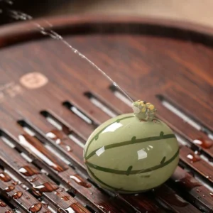 Watermelon frog tea pet spraying water on a tea tray, demonstrating interactive function