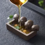 handmade Yixing purple clay lucky pig tea pet with tea being poured over it on dark tea table