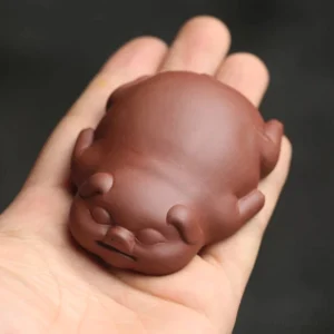 Handheld view of reddish-brown handmade Yixing purple clay cute pig tea pet showing palm size