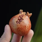 Handcrafted Yixing purple clay pomegranate tea pet on natural green background